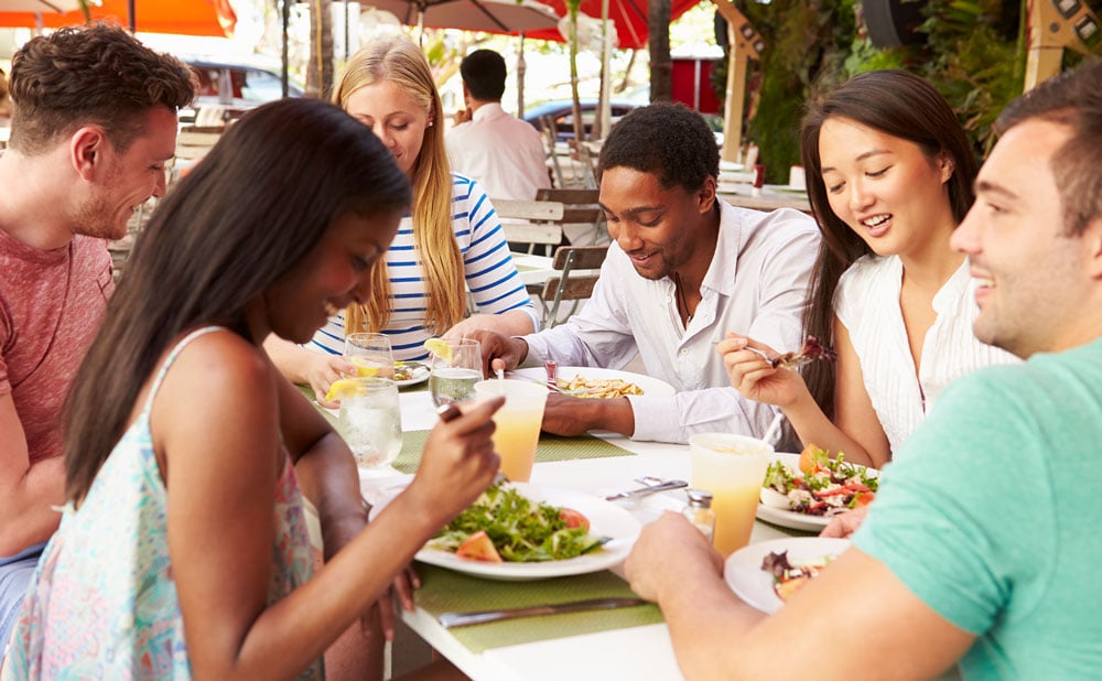 A group of people meeting and talking over lunch in an outdoor restaurant.
