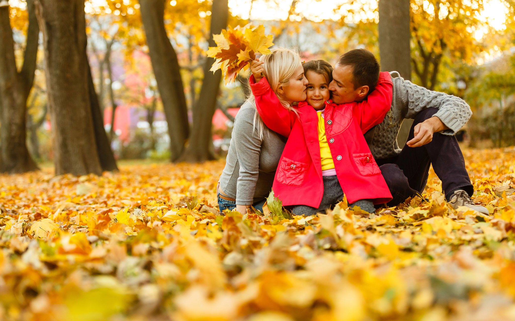 Happy family spending time together while resting on autumn orange leaves outdoor