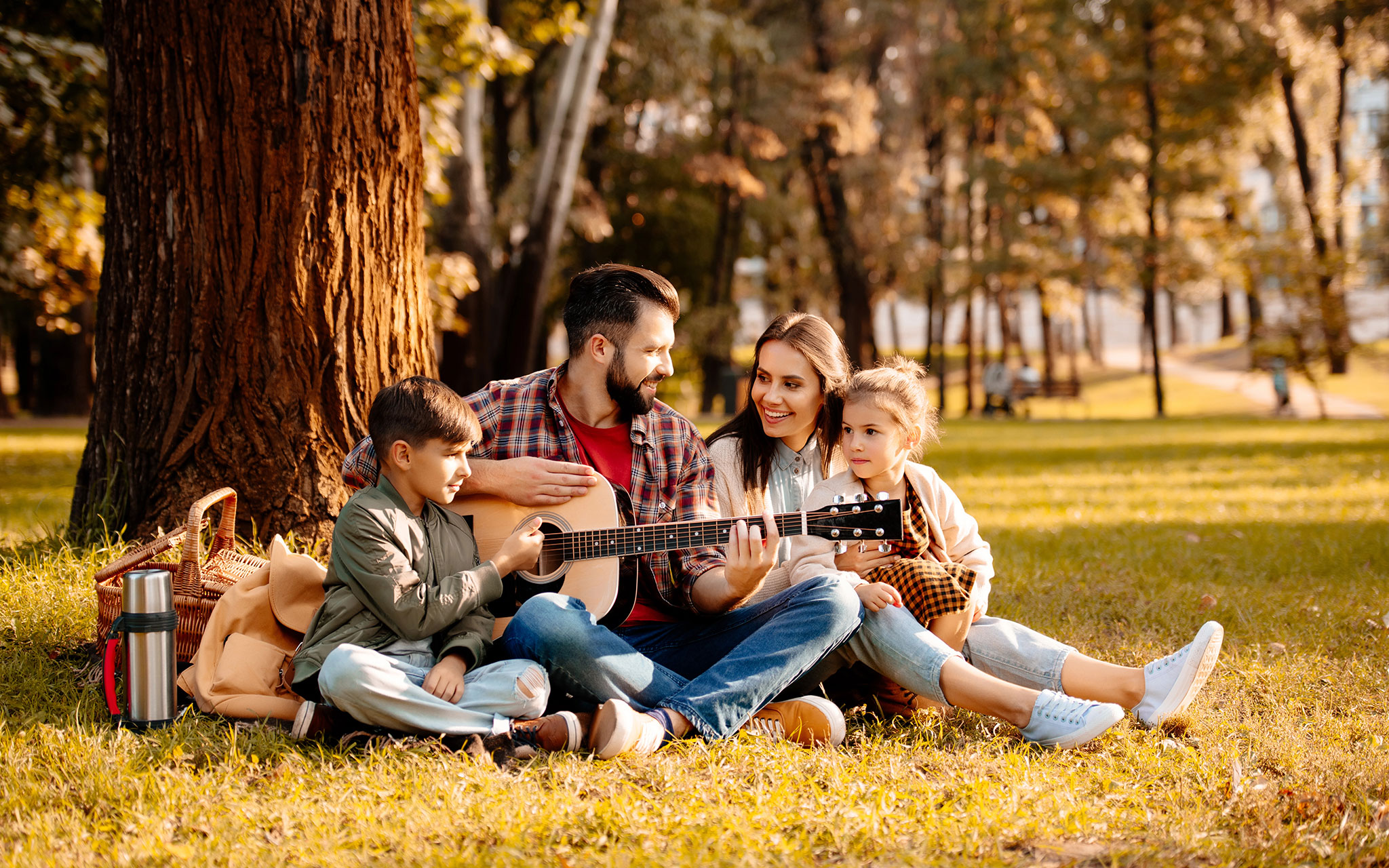 Family of four, mother, father, son, and daughter, on a picnic playing guitar