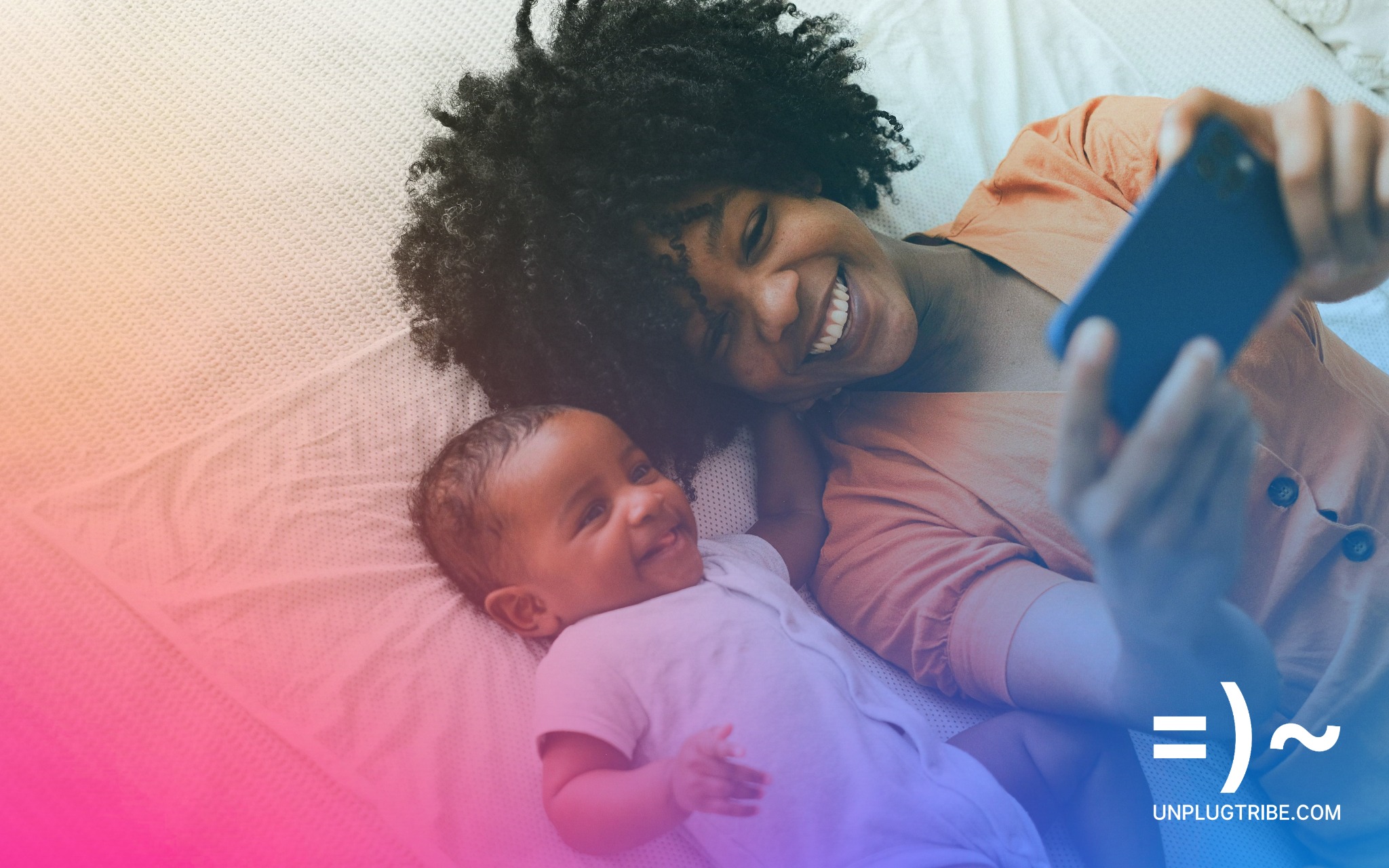 A toddler and mom lying on a bed at bedtime looking at a phone screen and smiling.